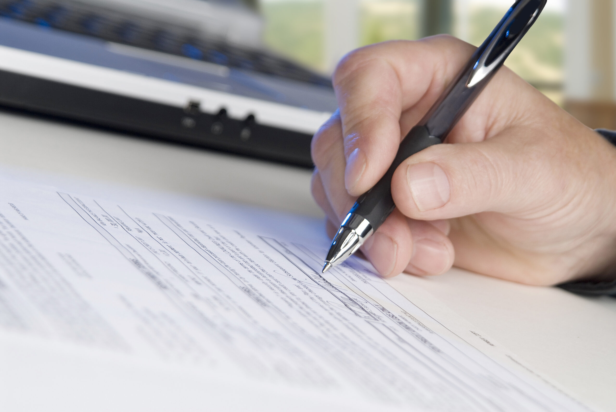 man signing papers, laptop, office windows in background